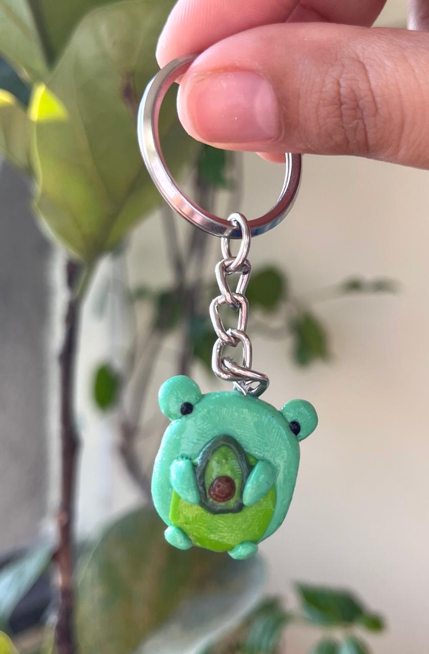 Green handmade frog keychain holding a tiny avocado